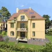 Außenansicht eines renovierten, dreistöckigen gelben Wohnhauses mit Satteldach und zwei Balkonen