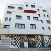 Weiße Wohnhausfassade mit geometrischen Fenstern und auffälliger Musterbemalung im Erdgeschoss.