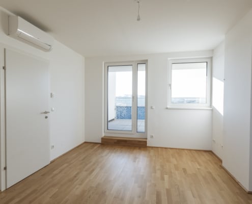 Der Wohnraum hat einen hellen Parkettboden. Das Fenster und die Terrassentür sind mit einme weißem Rahmen ausgeführt.