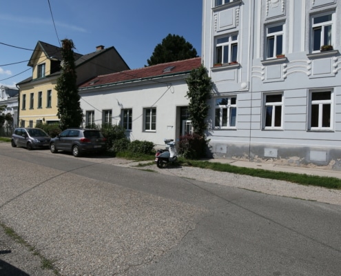 Hier sieht man mittig, zwischen einem Haus mit gelber und hellgrauer Fassade ein kleines Haus mit weißer Fassade