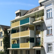 Man sieht zentral ein Haus mit beigen und petrolfarbenen Balkonen.