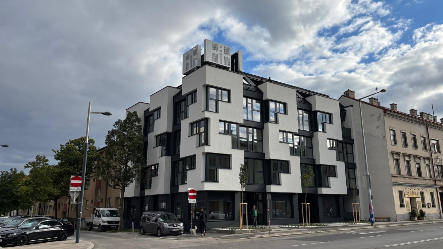 Hier sieht man ein Eckhaus mit weißer Fassade mit einer Terrasse im Dachgeschoß.