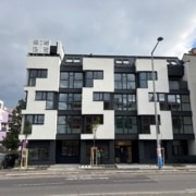 Hier sieht man ein straßenseitiges Haus mit heller Fassade und dunklen Fensterrahmen.