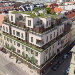 Man sieht ein saniertes Haus mit heller Fassade und braunen Elementen. Das Dach ist begrünt.